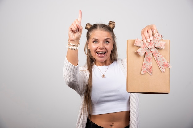 Cheerful woman showing gift and pointing at upside.