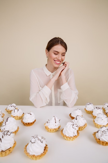 Free photo cheerful woman sitting at the table with cupcakes and smiling