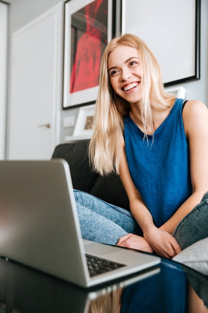 Donna allegra che si siede e che per mezzo del computer portatile a casa