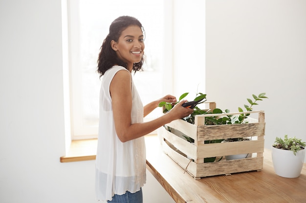 白い壁と窓の上の植物の茎をカットする準備を笑顔の陽気な女性