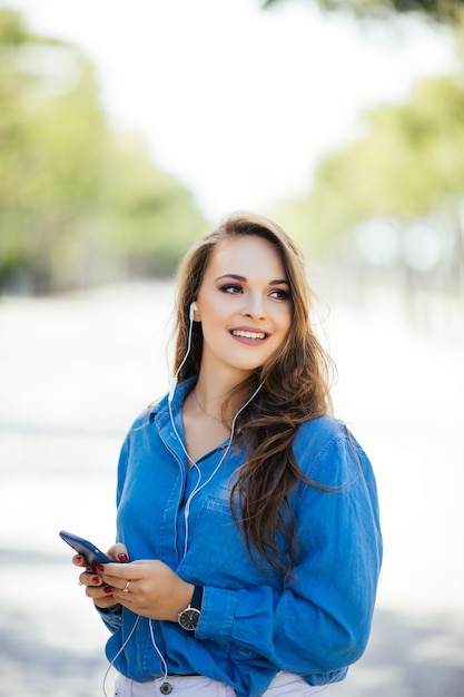 通りの陽気な女性は彼女のスマートフォンを使用しています。路上で電話を使用して若い実業家。