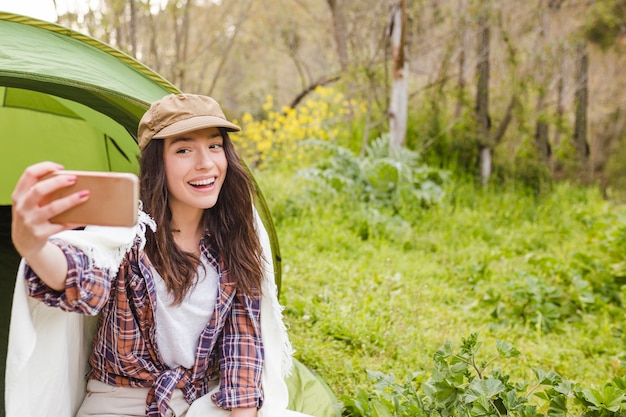 Free photo cheerful woman taking selfie near tent