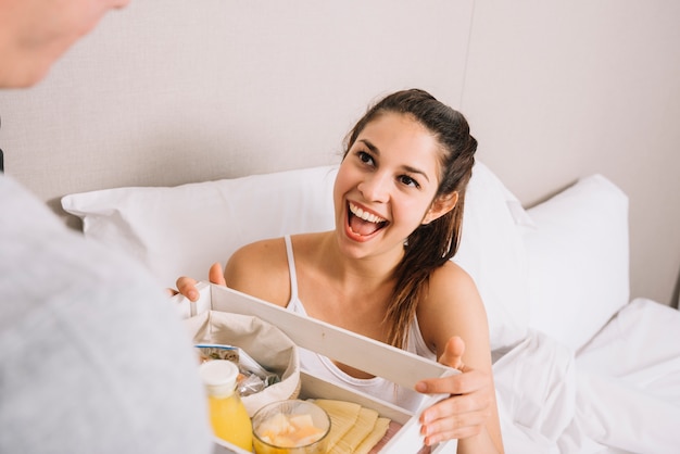 Foto gratuita donna allegra che prende vassoio con colazione a letto