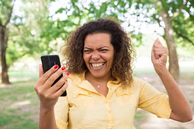 Cheerful woman using smartphone in city park