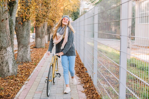 Cheerful woman walking with bicycle near fence