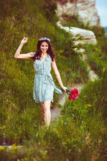 Cheerful woman walks with red bouquet arond green hill