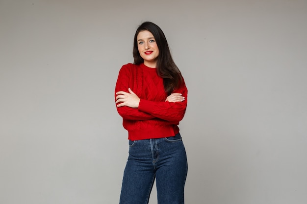 Una donna allegra con un caldo maglione rosso e jeans blu incrocia le mani sul petto