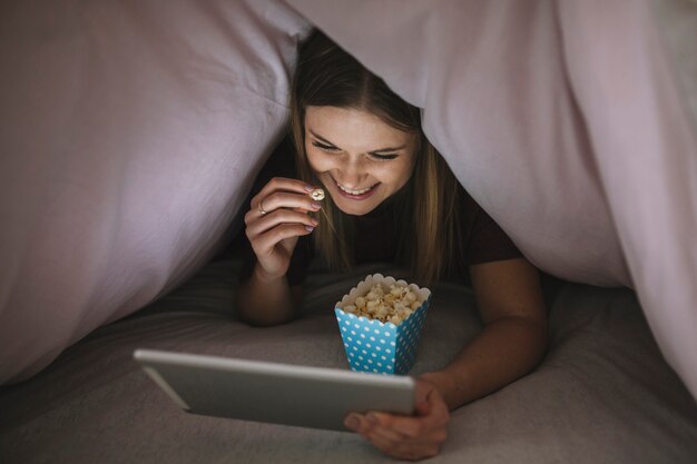 Cheerful woman watching film in blanket tent