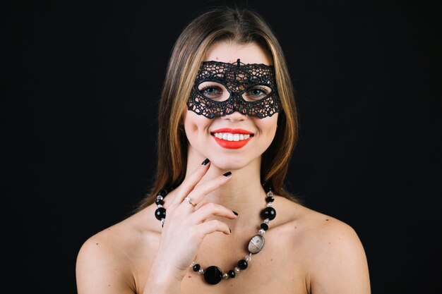 黒の背景上のカーニバルマスクとネックレスを着て陽気な女性