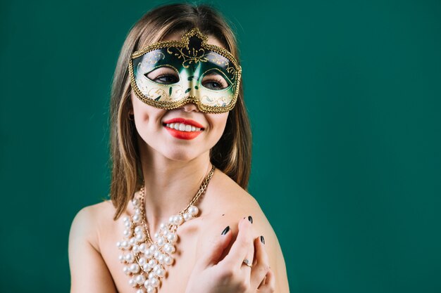 Cheerful woman wearing green carnival mask and necklace