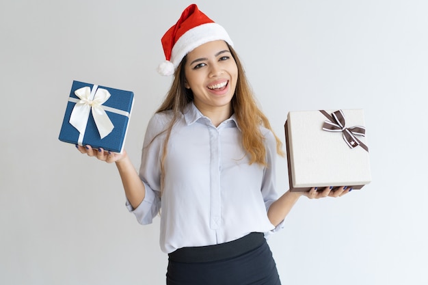 Donna allegra che indossa il cappello di babbo natale e mostrando scatole regalo