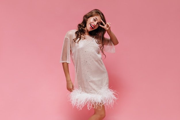白いドレスを着た陽気な女性はピンクの壁に広く笑顔