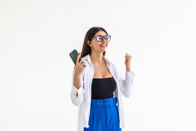 Cheerful woman winning on mobile phone making money in smartphone app and smiling standing happy on white background