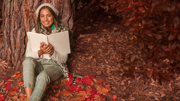 Foto gratuita donna allegra con il libro che si siede nella foresta