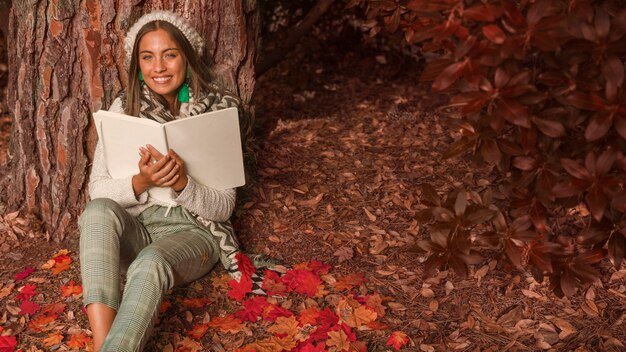 숲에 앉아 책을 가진 쾌활 한 여자