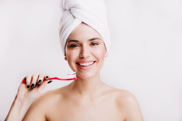 きれいな肌を持つ陽気な女性は、孤立した壁に笑っています。頭にタオルを持った女性が歯を磨くつもりです。