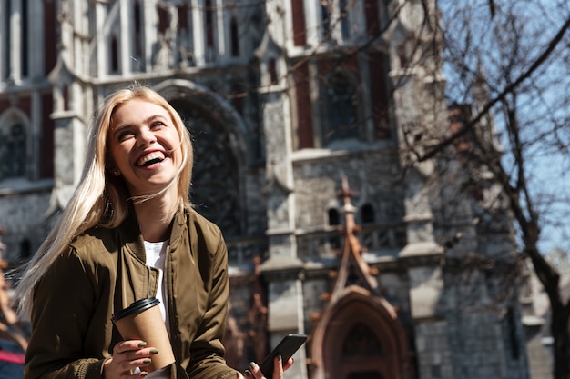 Cheerful woman with cup of coffee and smartphone laughing