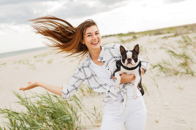 海の近くの週末を楽しんでいるかわいいボストンテリア犬と陽気な女性。女性のダンスと楽しい時を過します。