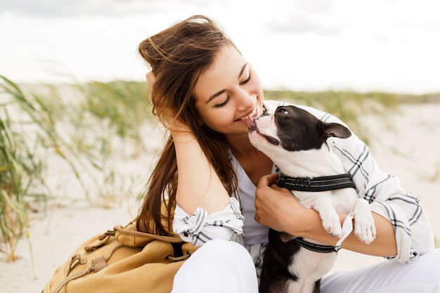 Cheerful woman  with cute boston terrier dog enjoying weekend near ocean.