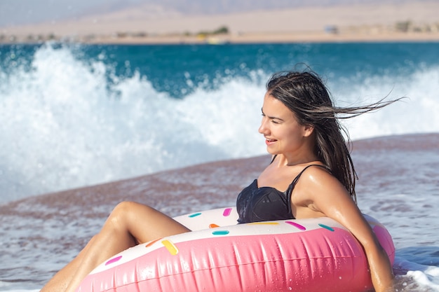Жизнерадостная женщина с плавательным кругом в форме пончика на берегу моря. Концепция отдыха и развлечений на отдыхе.