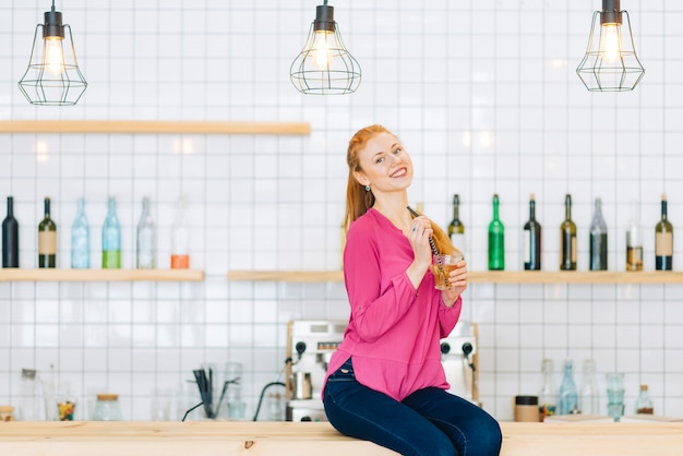 Cheerful woman with drink sitting on counter