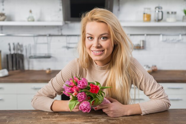 Cheerful woman with fresh flowers in kitchen 