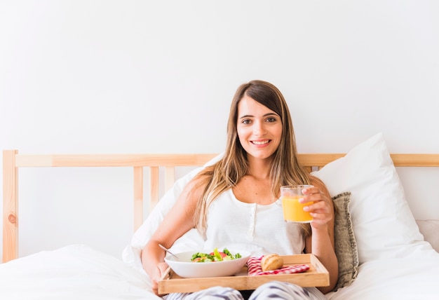 Cheerful woman with healthy food on bed