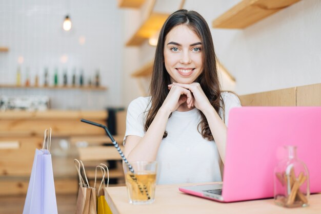 Cheerful woman with laptop in cafe after shopping
