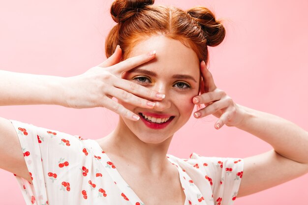 Cheerful woman with red hair looks into camera with smile. Portrait of woman in white T-shirt on pink background.