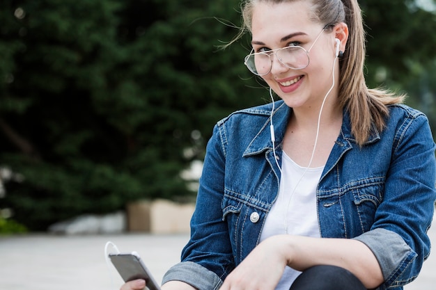 Foto gratuita donna allegra con lo smartphone che si siede sul marciapiede