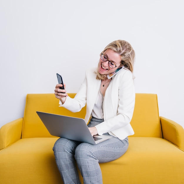 Cheerful woman with smartphones using laptop