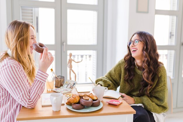 Cheerful women drawing and eating pastry