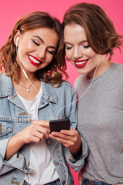 Cheerful women friends using mobile phone listening music.