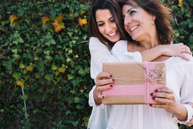 Cheerful women with gift hugging in garden