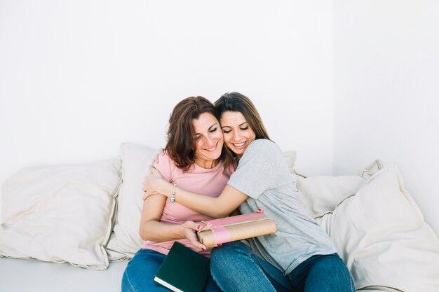 Cheerful women with present hugging at home