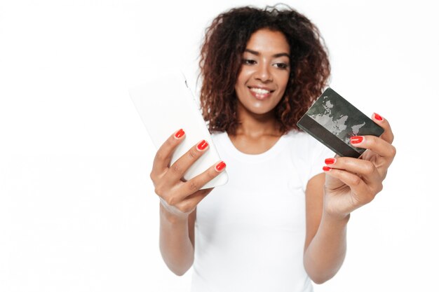 クレジットカードを保持している電話を使用して陽気な若いアフリカ女性。