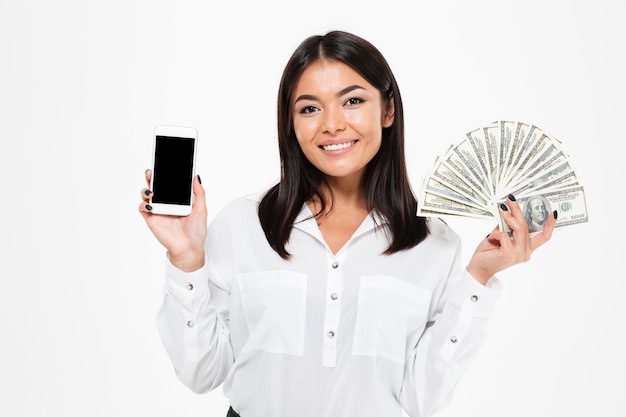 Free photo cheerful young asian woman holding money showing display of phone.