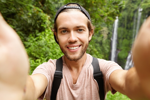 エキゾチックな国での休暇でselfieを取って野球帽をかぶっている陽気な若いひげを生やしたヒップスター