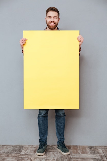 Cheerful young bearded man holding blank board