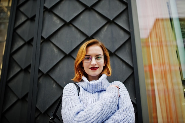 Cheerful young beautiful redhaired woman in glasses warm blue wool sweater with backpack posed outdoor