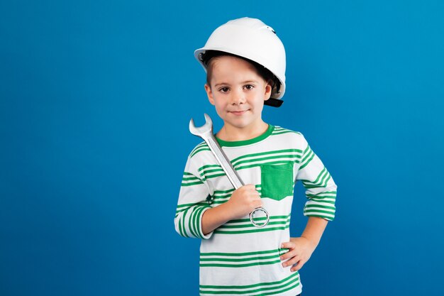 Cheerful young boy in protective helmet posing with wrench