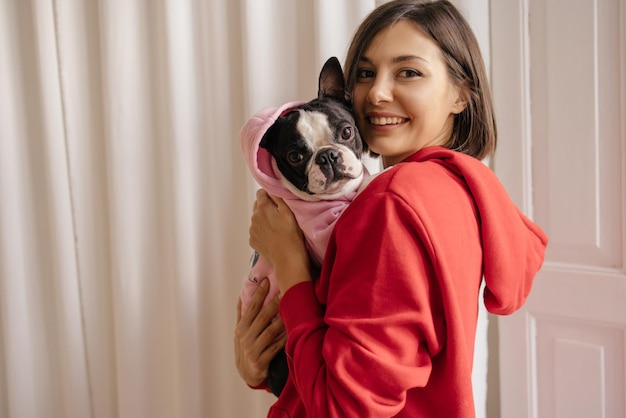 無料写真 屋内で彼女の犬を腕に抱いている陽気な若いブルネット白人女性犬の世話の概念