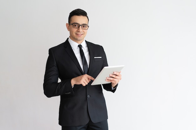 Cheerful young businessman checking email on tablet and looking at camera. 