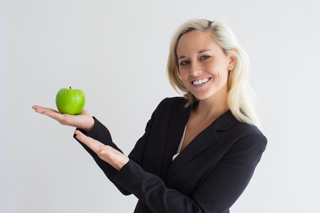 Cheerful young businesswoman showing green apple