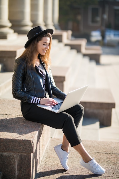 Cheerful young businesswoman student girl works with her brand laptop computer in the city centre