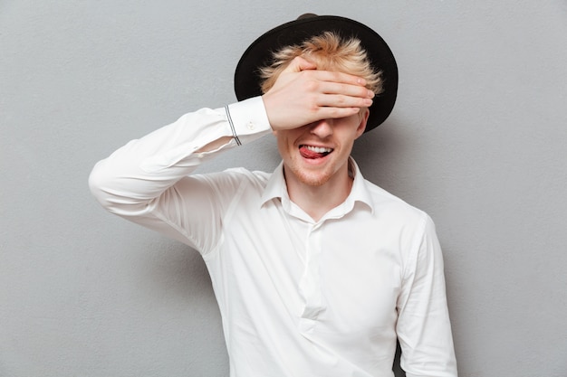 Cheerful young caucasian man covering eyes with hand