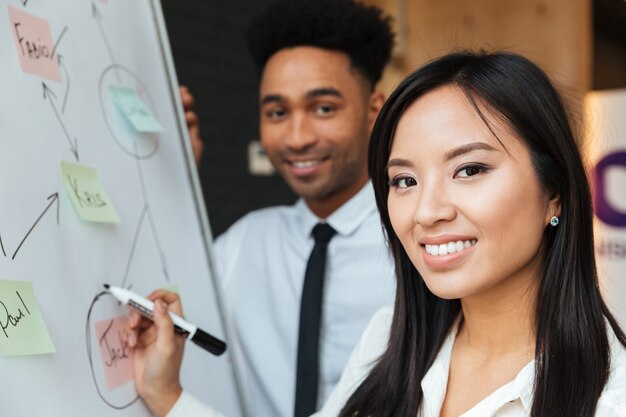 Cheerful young colleagues write something with marker