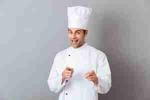 Free photo cheerful young cook in uniform pointing to you.