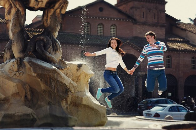Cheerful young couple jumps before fountain somewhere in Rome