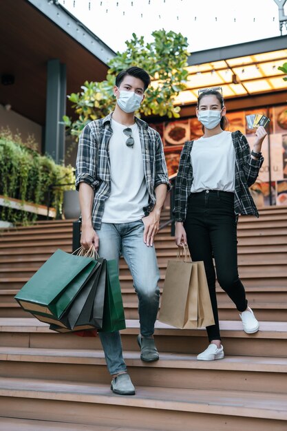 Cheerful young couple in mask holding multiple paper shopping bag